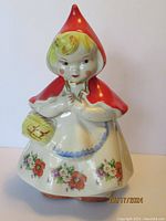 Front view of the ceramic cookie jar showing the Little Red Riding Hood figure in red hood and floral dress.