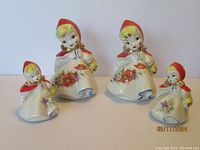Four vintage ceramic salt and pepper shakers styled as Little Red Riding Hood, showing two sizes with detailed floral painting and red hooded capes