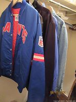 Side view of three jackets on hangers including the blue Giants NFL Chereskin jacket, dark leather jacket, and light denim jacket.
