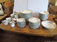 All items displayed on wooden table, showing large stack of plates and cups with saucers.