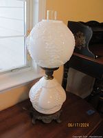 Side view of the vintage Victorian double globe electric lamp showing upper and lower globes of white milk glass with grape cluster pattern and ornate metal base.