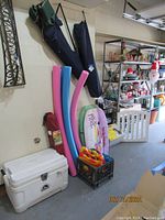 Wide shot showing all items in lot: cooler, pool noodles, boards, camp chairs, crate with water toys.