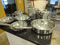 Overview photo showing multiple stainless steel pots and pans including fry pans and stock pots on a black countertop.