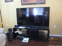 60 inch Sharp Aquos LCD TV on black media console with Bose speaker to the side, showing overall setup and scale.