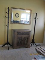 Full view of the storage cabinet with metal scrollwork, two coat racks on either side, and wall mirror on the wall above.