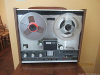 Front view of vintage TEAC 1230 stereo reel-to-reel tape deck showing control panel, meters, knobs, and reels mounted on metal front with wooden side panels.