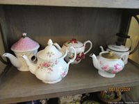 Shelf display of five decorative teapots with floral and fruit motifs, showing overall lot contents