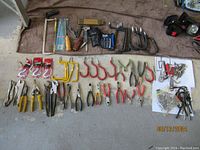Overview of assorted hand tools including various pliers, clamps, screw hooks, and hardware pieces laid out on a towel.