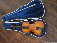 Open violin case showing violin and bow inside laid on blue plush lining.