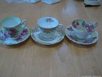 Photo showing set of 3 cups and saucers with distinct floral designs and gold edges.