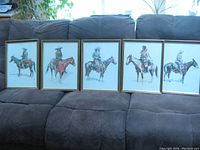 Five framed Frederic Remington prints lined up on couch showing Old West mounted figures
