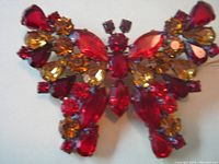 Close-up image of the butterfly pin showing detailed setting and arrangement of red and amber stones.