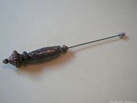 Full view of the antique hat pin showing the entire length with metal decorative handle and stopper on the tip