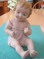 Front view of seated bisque baby figurine in pink-trimmed outfit, showing facial features and posture