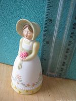 Photo of the porcelain bell figurine shown next to a ruler for size reference, measuring about 3 1/4 inches tall.