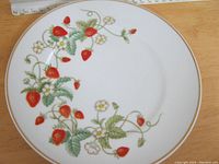 Top view of round porcelain sandwich plate decorated with strawberries and blossoms, gold trim around edge, includes a ruler for scale