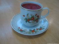 Demitasse cup filled with a red wax candle, showing strawberry pattern with gold trim