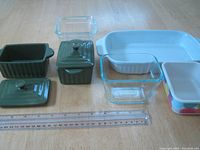 Photo showing white ceramic oval baking dish, two clear glass square baking dishes (one with lid), multicolor ceramic rectangular baking dish with lid, and a green ceramic container.