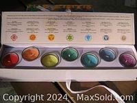 Top-down view of 7 chakra candles arranged in color sequence with a printed chart explaining each chakra above them.