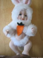 Full view of the porcelain baby doll dressed in a white fluffy bunny costume with a carrot decoration on the chest, showing the articulated movable limbs and overall condition.