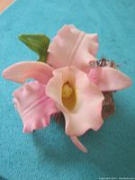 Front angle view of the pink porcelain orchid sculpture showing detailed petals and green leaf attached to bark-like base.