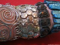 Close-up of bracelets showing wire spiral, hammered discs, black stones, and blue pieces