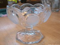 Clear crystal candy dish with scalloped edges and pedestal base, showing compressed beaver coin pattern on the bowl.