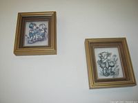 Two framed German Hummel paper tole artworks shown side by side from front view, one slightly faded.