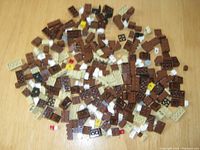 Scattered assortment of LEGO bricks including brown, beige, white, black, grey, red, and yellow colors, shown on wooden surface.