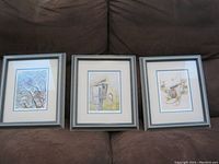 Three framed prints side by side on a brown couch showing overall lot contents.