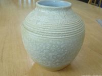 Full view of off white pottery vase with light gold tone and round shape on wooden surface.