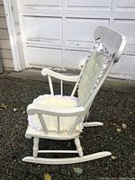 Side view of solid white wooden rocking chair with yellow cushion, showing turned legs and curved rockers
