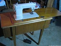 Singer sewing machine mounted on wooden cabinet with drawers, showing scratches and stains on cabinet surface