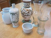 Six assorted vases of varied sizes including porcelain with bamboo design, ornate ceramic with gold and green leaves, clear glass, and white ceramic varieties