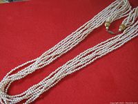 Four-strand vintage pearl necklace shown on a red background, displaying the full length of the strands.
