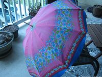 Closed view of the umbrella laid open showing the pink floral canopy with wood stock and metal handle on a patio.