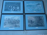 Four WW1 prints in black frames with blue matting arranged on floor, showing various war scenes