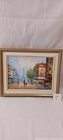 Framed oil painting showing a street in Paris with buildings, people walking, and the Eiffel Tower in the background.