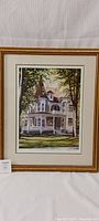 Framed print showing a large Victorian house in a landscaped setting, with the frame and matting visible.