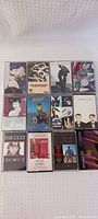 Front view of 13 assorted music cassette tapes in their cases showing cover art from various artists including Madonna, The Cult, and Pink Floyd.