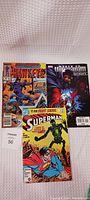 Photo showing three comics: Hawkeye, March of the Ultimum Saga, and Superman on a white textured background.