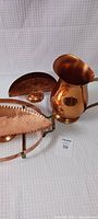 Photo showing copper pitcher, glass dish holder with copper base, and copper decorative napkin/letter holder on white background.
