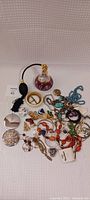 Collection of assorted costume jewellery and large perfume sprayer displayed on white textured background.