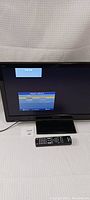 Photo shows Panasonic TV monitor powered on with 'Input select' menu visible on screen. Black bezel with Panasonic logo, TV on stand, remote in front.