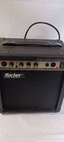 Front view of Rocker RA-100 guitar amplifier showing control panel and brand name.