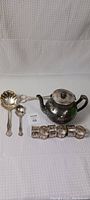 Full view of set including teapot, 5 napkin rings, 2 serving spoons and scissors showing condition and arrangement