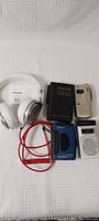 Overview of all lot items including headphones, portable recorders, cassette player, and flip phone on white background