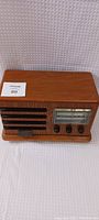 Front and side angled view of the wooden radio showing tuning knobs, frequency dial, and speaker grille.