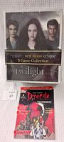 Front view of Twilight Saga 3 Game Collection board game in shrink wrap showing main characters and Dracula comic book with sealed cover.