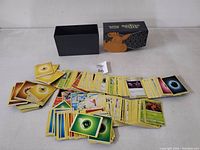Top view of Pokémon trading cards spread next to black and orange themed Pokémon card box